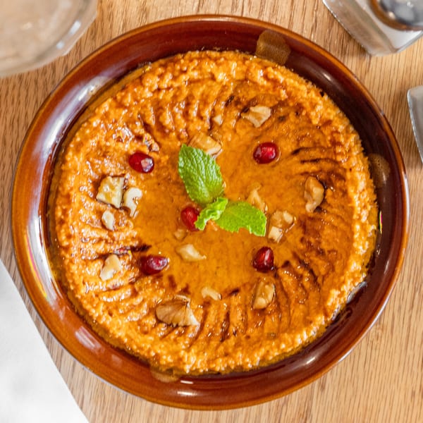 A rich orange dip topped with walnuts, pomegranate seeds, and fresh mint on a wooden table.