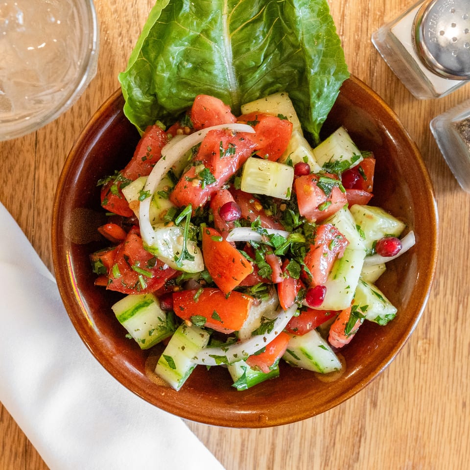Vibrant tomato, cucumber, and onion salad with herbs and pomegranate on a wooden table.