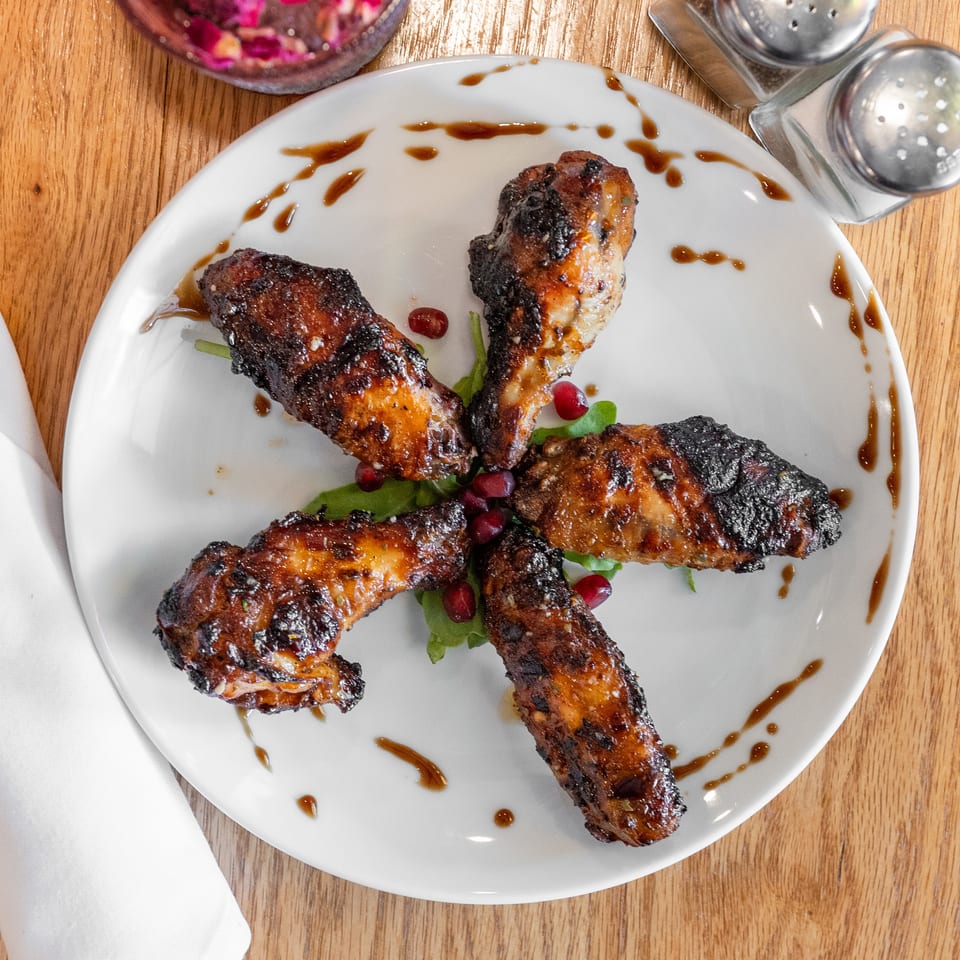 Five glazed chicken wings with pomegranate and greens on a white plate, on a wooden table.