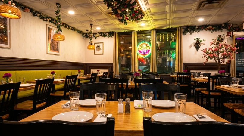 Inviting restaurant dining room with wooden tables, green banquettes, floral decor, and a neon window sign.
