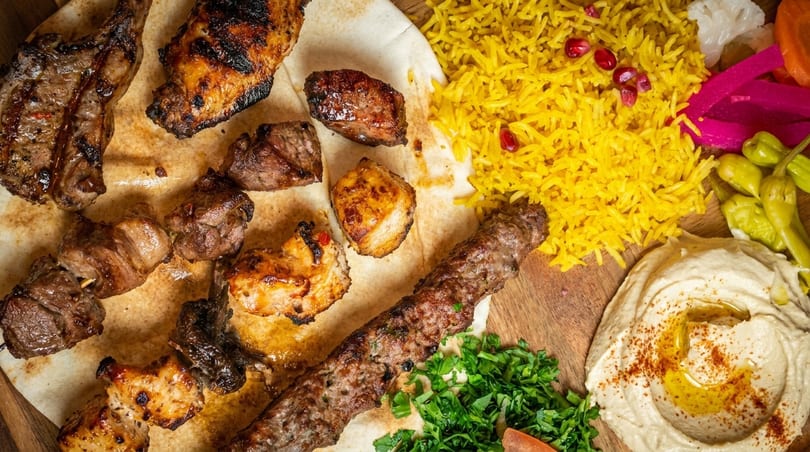 Grilled meat platter with kebabs, lamb chops, yellow rice, hummus, and pickled vegetables.