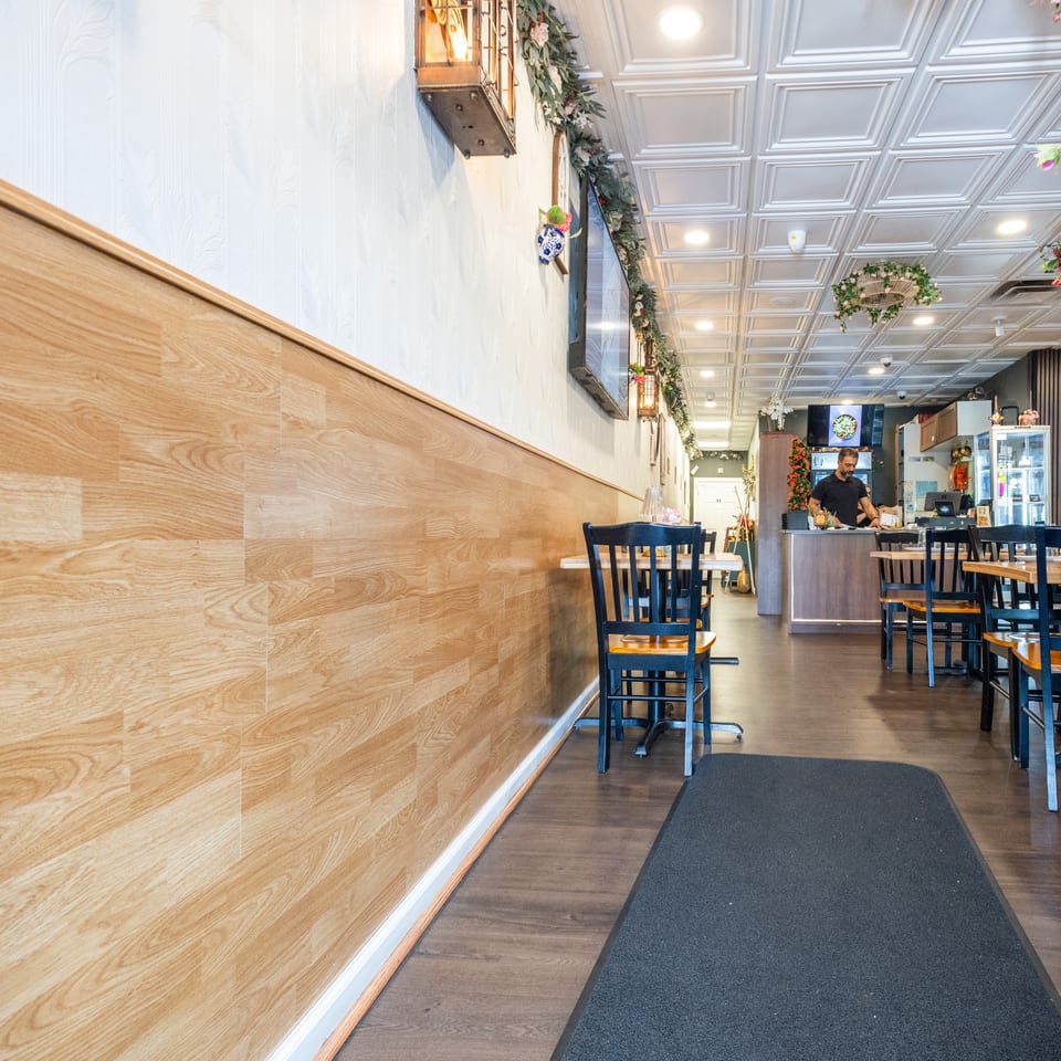 Bright restaurant interior with wooden paneling, dining tables, and a server at the counter.