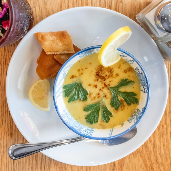 Creamy yellow soup garnished with parsley and lemon, served with pita bread on a white plate.