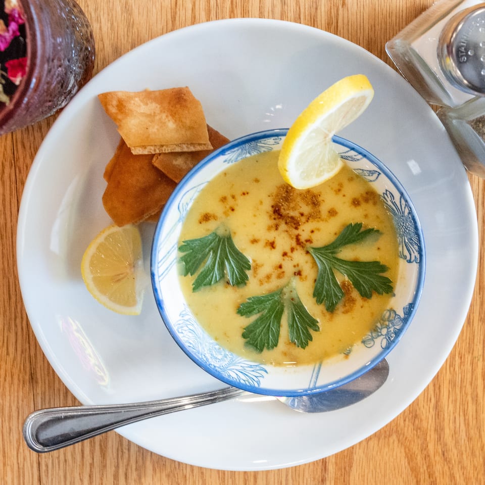 Creamy yellow soup garnished with parsley and lemon, served with pita bread on a white plate.